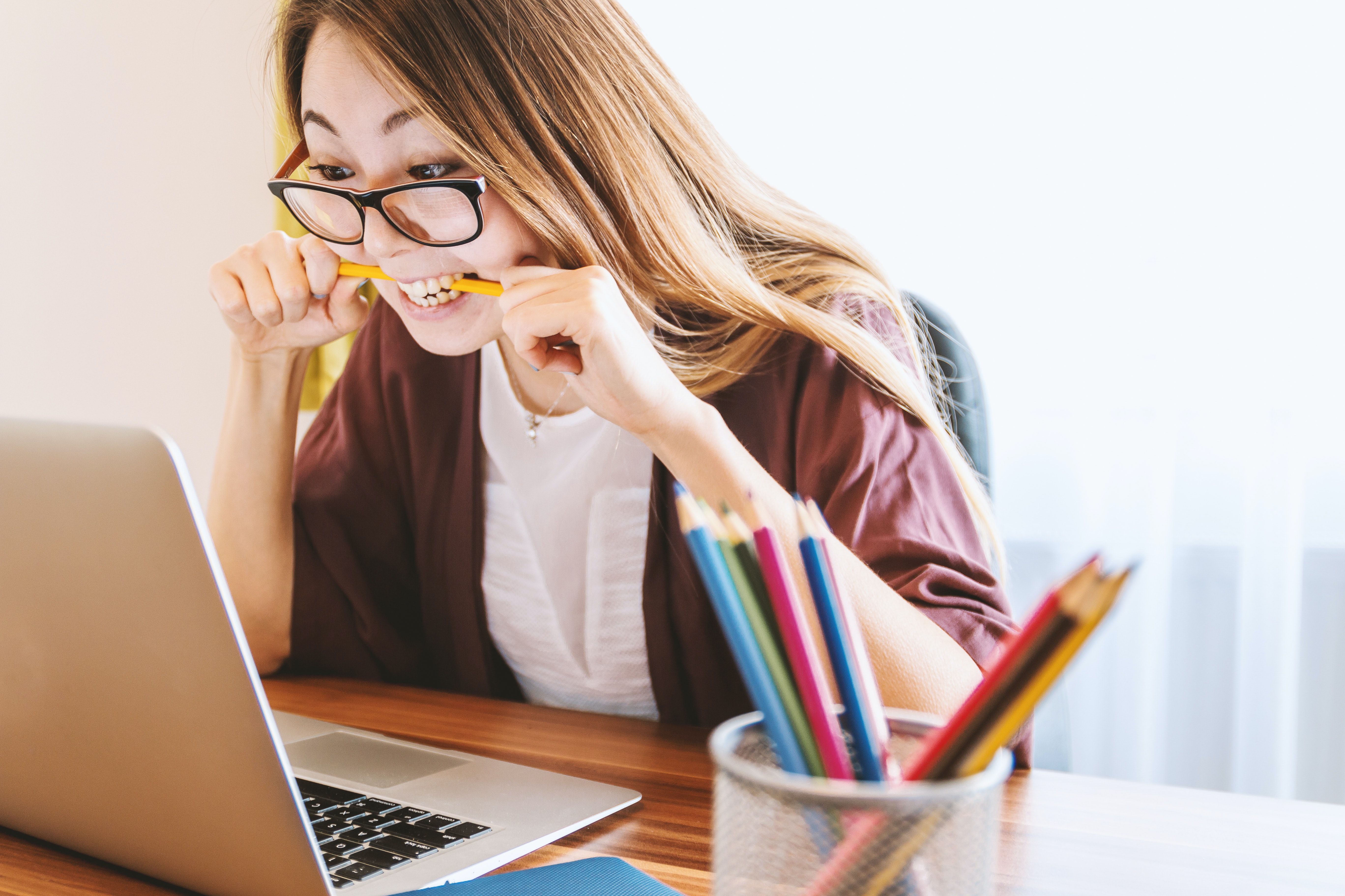 A girl bitting a pencil and looking at the computer screen